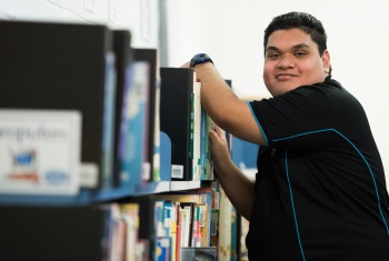 Participant stands beside a bookshelf with his arm resting on a book