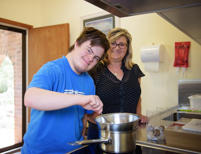 20-year-old NDIS participant Ben, stirring a pot on the stove with his mum behind him overseeing his progress.