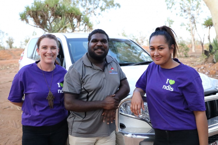 Andrew stands beside the car with two women in purple t-shirts