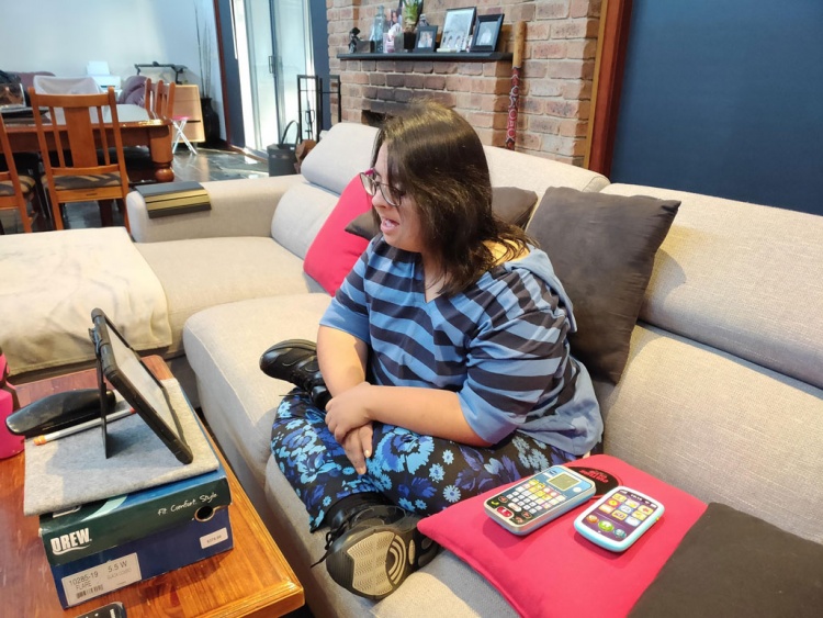 Casey sits on her couch, having a video call with her iPad in front of her