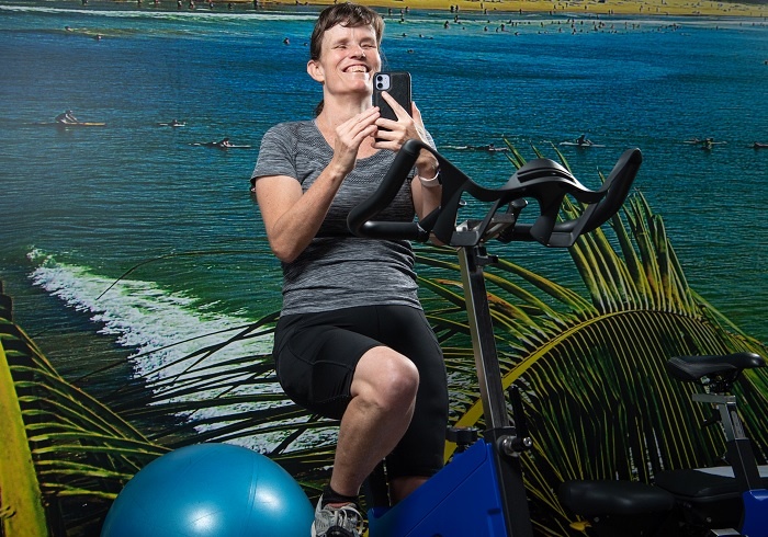 Chrystal on an exercise bike and holding a mobile phone