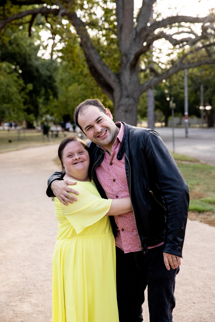 Smilng couple - a young woman in a yellow dress and her smiling boyfriend who has his arm around her