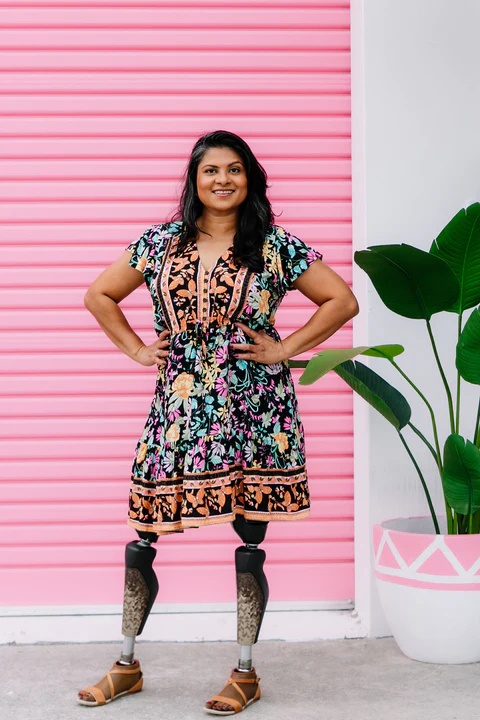 Smiling woman standing on prosthetic legs posing in front of a pink wall