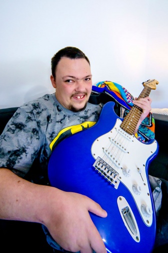 Christopher plays his blue electric guitar in his share house