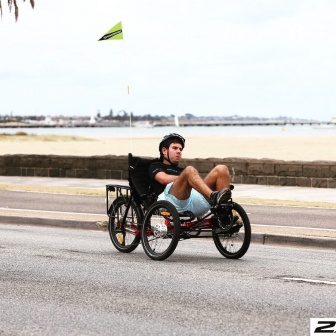 Tom riding his recumbent trike on the road next to a beach