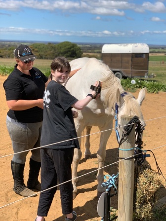 Brett smiles at the camera while brushing down a horse