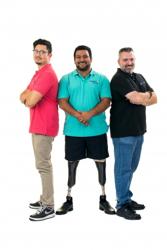 Three men standing together. The men on the left and right are facing outwards with their arms crossed, the man in the middle has prosthetic legs and is facing towards the camera.
