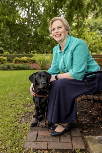 A woman is sitting on a park bench smiling next to her guide dog