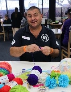 Geoff is sitting at a table with yarn doing a craft activity