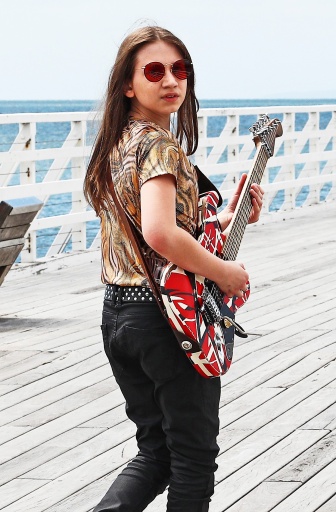 Jaybird walking along pier with a guitar in hand. Her face turns back towards the camera.