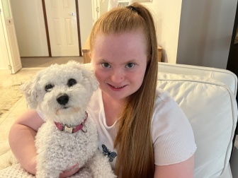 A smiling Alyssa with her arm around a small white dog.