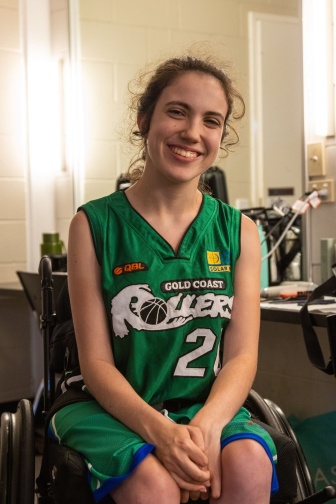 Smiling young woman wearing a green basketball uniform and sitting in a wheelchair