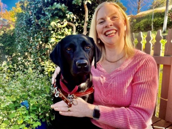 Donna sitting outside with her arms around a black labrador 