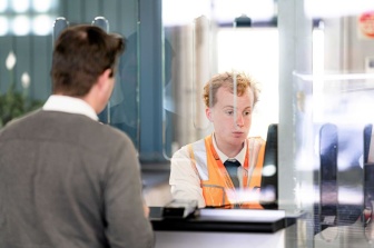 Henry John behind the train station counter serving a customer