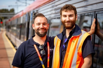 Two men stand in front of a train, one is wearing a driver high vis vest
