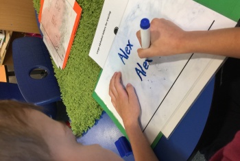 Looking over the shoulder of a six-year-old NDIS participant, utilising Early Childhood Early Intervention supports through his NDIS plan, practicing to write his name.