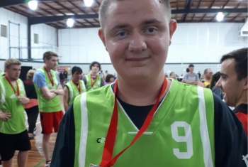 NDIS participant James is wearing a green jersey with the number nine on it. It's part of his pool playing competition uniform. He is proudly wearing a medal around his neck. He is smiling at the camera.