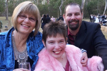 Lacey and her parents at an outdoor wedding, they are dressed up, Lacey has a champagne glass in front of her