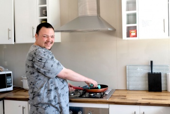 Christopher happily using newly found skill of cooking on his stove in his share house kitchen