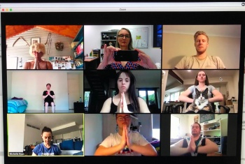 A TV screen displays 9 squares with people in it, joining in a virtual dance class from their own homes