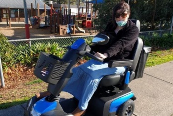 Belinda sitting on her blue scooter looking at the camera