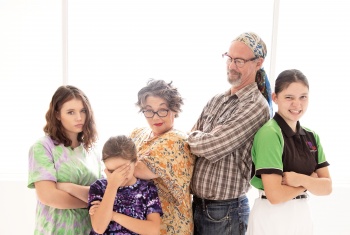 Two adults standing with their arms crossed in an amusing way, they're surrounded by 3 young teenage girls who also have their arms crossed.