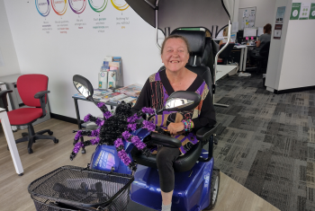 A woman is sitting on a mobility scooter with a large glittery spider on the front.