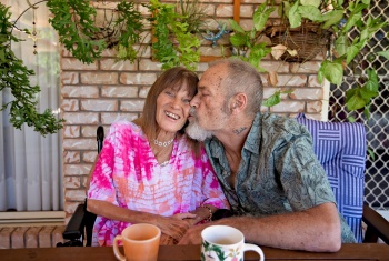 Man sitting beside his smiling wife and gives her a kiss on the cheek