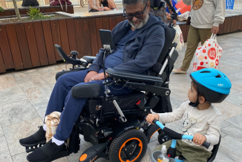 Kemal in wheelchair smiling down at a small boy in a tricycle next to him