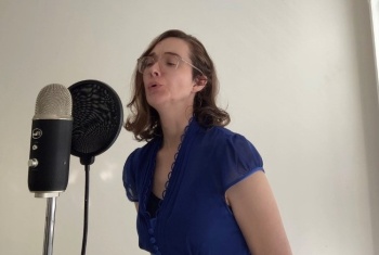Olivia singing into a microphone while wearing a dark blue dress