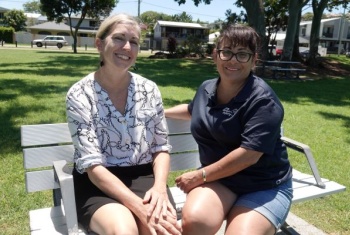 Angela is sitting on a bench outside in a park with Gemma
