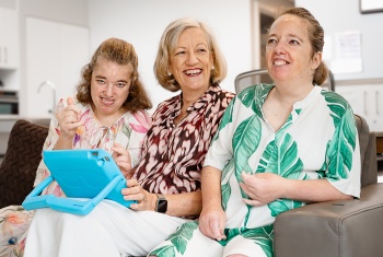 Mum Mary-Ellen (centre) sits on a couch with twin daughters Georgia and Ellen.